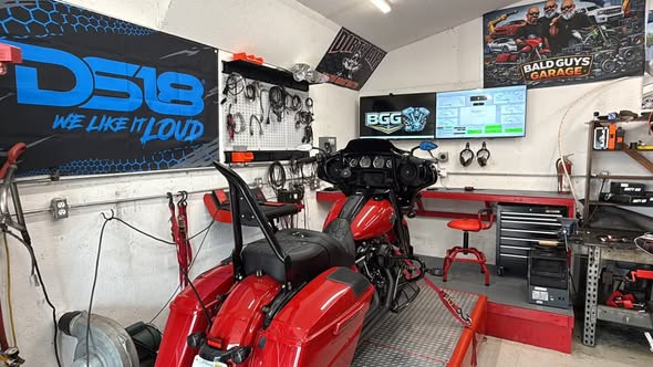 A red touring motorcycle secured on the Bald Guys Garage dynamometer inside the BGG workshop